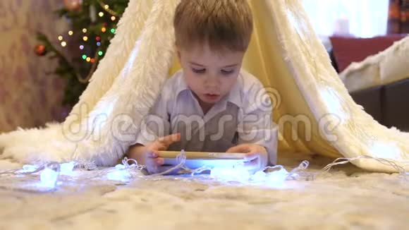 孩子们在孩子们的房间里玩智能手机在一个带有圣诞灯的帐篷里快乐的童年视频的预览图
