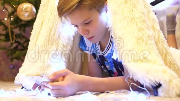 这个少年在孩子们的房间里玩智能手机帐篷里放着圣诞灯快乐的童年视频的预览图