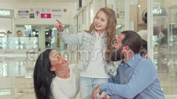 可爱的小女孩指着商场的服装店和她的父母一起购物视频的预览图