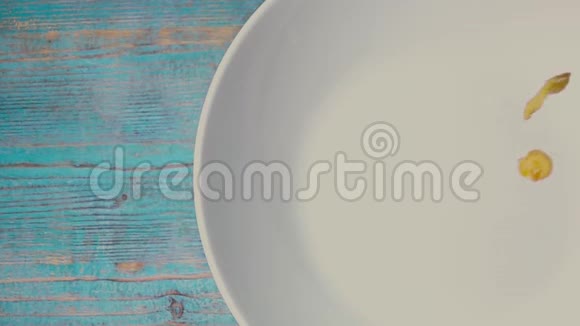 在蓝色木桌上的盘子上浇玉米片自上而下的超级慢镜头视频的预览图