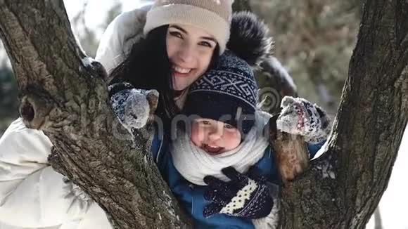 一位年轻的母亲和她的儿子在冬天在一个白雪覆盖的公园里的树枝上画了34年视频的预览图