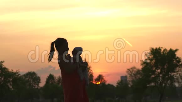 夕阳的剪影年轻的母亲抱着她的小男孩在城市公园站在夕阳面前生动活泼视频的预览图
