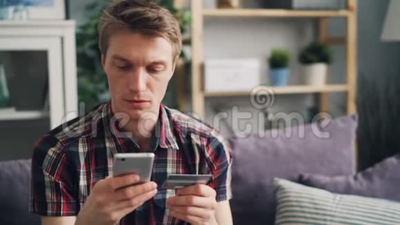 帅哥在网上购物用信用卡支付用智能手机触摸屏幕然后微笑着看视频的预览图