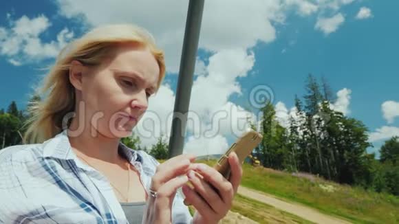 一个年轻的女人使用智能手机在晴朗的夏日乘坐滑雪电梯视频的预览图