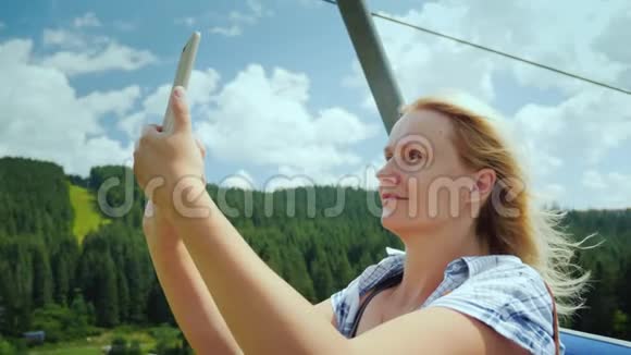 一位活跃的妇女在一个滑雪电梯的小屋里拍摄美丽的山脉和森林景色假期视频的预览图