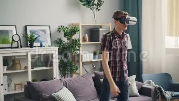 兴奋的家伙正在玩虚拟现实护目镜戴着耳机一个人站在房间里移动手臂视频的预览图