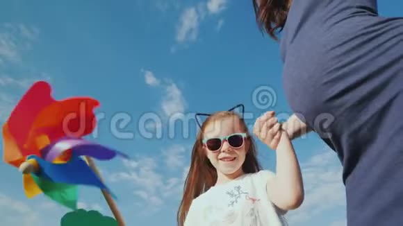 一个快乐的女孩在她怀孕的母亲身边玩玩具风车视频的预览图