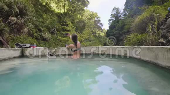 旅游妇女使用手机自拍照片在矿物浴从温泉在户外水疗旅游博客写手视频的预览图