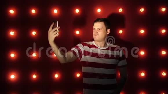 年轻男性站在明亮的墙上在智能手机上自拍视频的预览图
