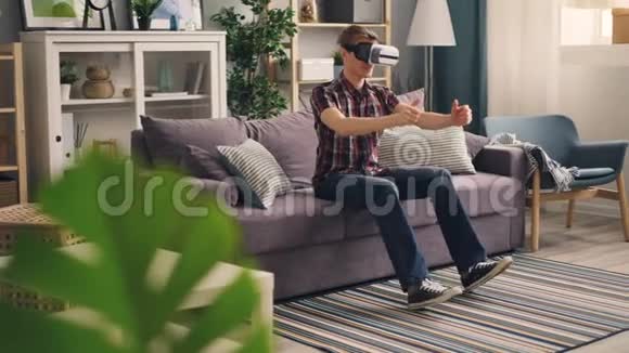 免费学生玩虚拟现实眼镜坐在沙发上驾驶赛车然后移动视频的预览图