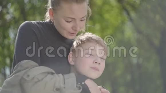 肖像年轻的母亲和她十几岁的儿子一起在公园里休息那个女人亲吻她的孩子的脸颊他亲吻视频的预览图