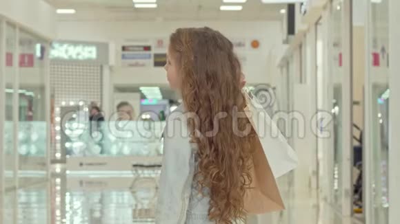 一个头发卷曲的小女孩在商场里看服装店的后景镜头视频的预览图