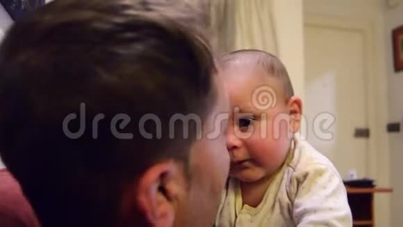可爱的睡眼的六个月大的小男孩揉着眼睛而爸爸正在和他说话试图让他保持清醒视频的预览图