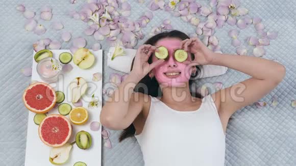 在健康中心英俊的女人躺在脸上脸上戴着粉红色的面具眼睛上戴着黄瓜视频的预览图