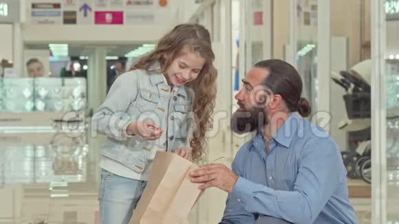 可爱的小女孩和她的父亲在商场里看着购物袋视频的预览图
