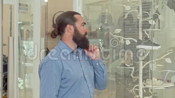 成熟的长胡子男人若有所思地看着服装店的陈列视频的预览图