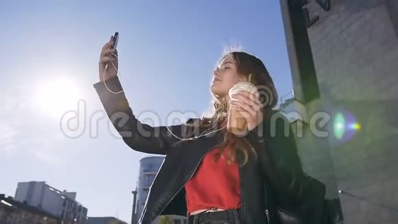 年轻漂亮的金发女孩在城市街头行走时在智能手机摄像头上自拍照片的画像视频的预览图