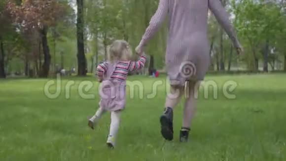 妈妈和小女儿牵着手在神奇的绿色公园里跑来跑去在公园里玩耍的女人和小孩视频的预览图