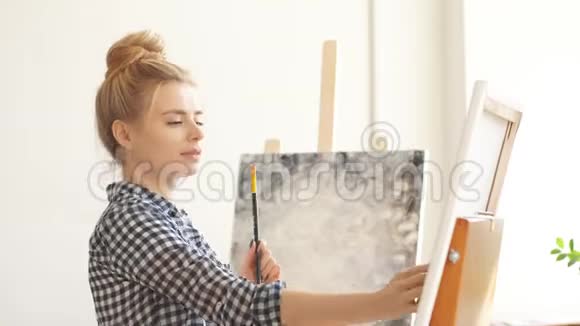 有趣的金发女孩手里拿着刷子用铲子纠正她的艺术作品视频的预览图