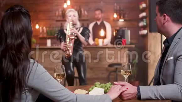 年轻夫妇在约会时为一位女萨克斯演奏家鼓掌视频的预览图