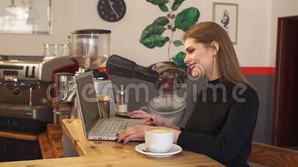 年轻女子在咖啡馆里喝着一杯卡布奇诺在电脑上写着文件视频的预览图