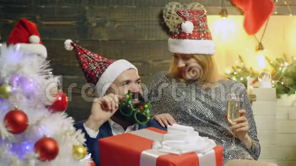 戴着新年帽子女孩坐在胡须男旁边手里拿着一个大红盒子里面放着新年背景礼物视频的预览图
