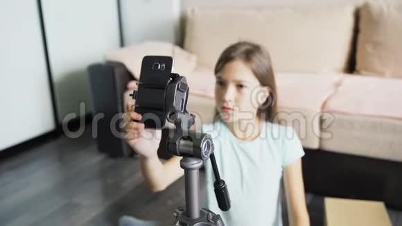 一个年轻女孩在三脚架上安装了一部智能手机用于在线广播女孩描述的是制造广告的设备视频的预览图