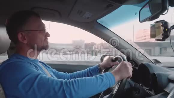 穿蓝色长袖的白人男子在背景上驾驶带有建筑物和其他汽车的汽车视频的预览图