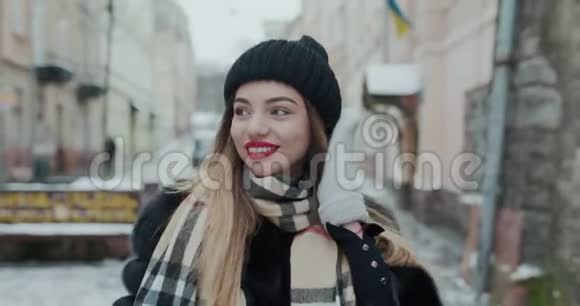 迷人的女孩穿着一件带红唇的黑色毛皮大衣在一个城市的街道上而不是转向相机和微笑视频的预览图