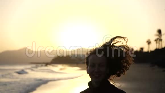 慢动作接近年轻女子在沙滩上慢跑的剪影头发随风飘动看着大海上的夕阳视频的预览图