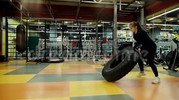 强壮的运动女性在健身房中缓慢地转动大型拖拉机轮胎视频的预览图