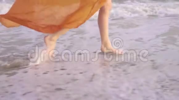 日落时女性光着脚和飘舞的裙子年轻的赤脚女孩穿着长长的橙色连衣裙沿着冲浪线奔跑视频的预览图