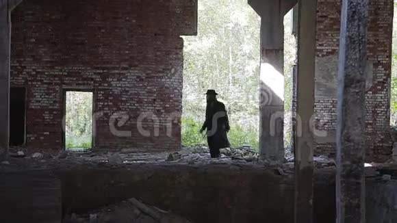 一个穿着黑色斗篷的硬汉在一个废弃的工厂或工厂里四处寻找某人视频的预览图