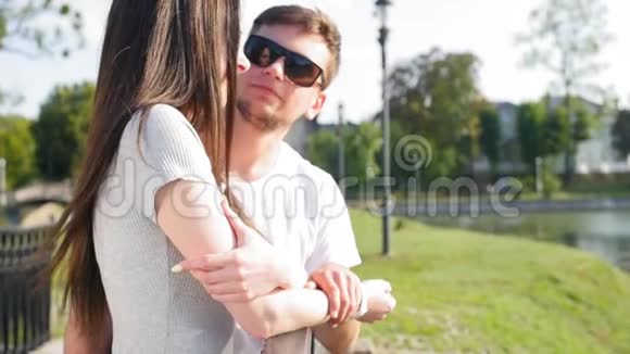 年轻漂亮的夫妇正站在桥上的公园里聊天男人调情拥抱女孩视频的预览图