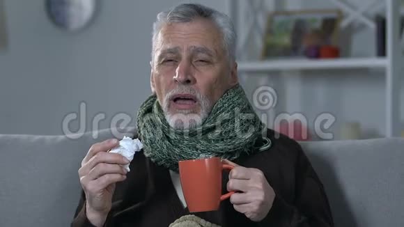 戴着围巾的老人在家喝热茶打喷嚏流感病毒视频的预览图
