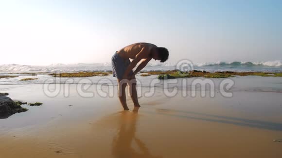 运动男子站在黄色的湿沙上缓慢伸展视频的预览图