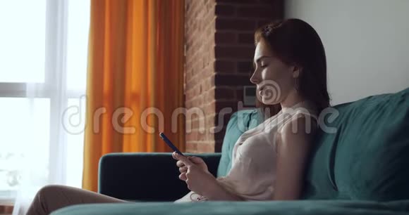 年轻女子坐在沙发上使用智能手机视频的预览图