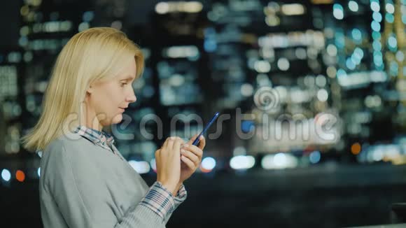 白人中年妇女在曼哈顿灯光的背景下使用智能手机侧视视频的预览图