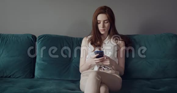 年轻女子坐在沙发上使用智能手机视频的预览图