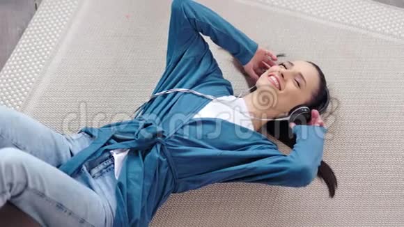 快乐可爱的年轻女性戴着耳机在地毯上高角度听音乐视频的预览图