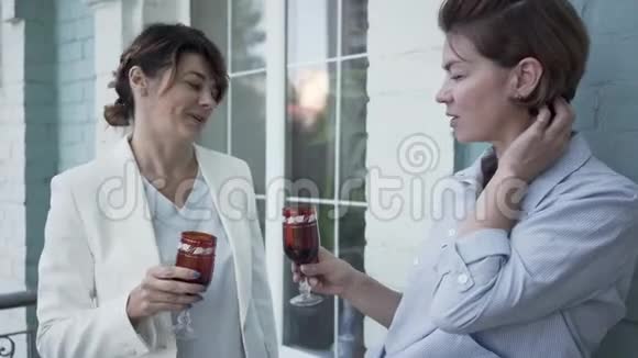 两个优雅的成年女朋友站在阳台上放松喝酒可爱的女人在家里在一起视频的预览图