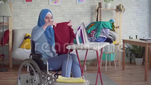 漂亮的穆斯林妇女坐轮椅做家庭作业熨衣服视频的预览图