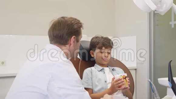 成熟的牙医一边和可爱的小男孩一起工作一边对着镜头微笑视频的预览图