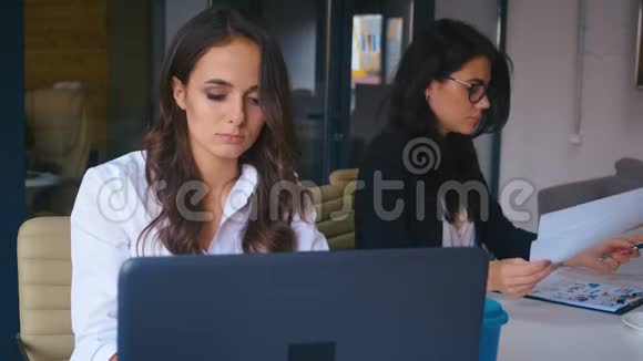 无聊的女商人坐在办公室的笔记本电脑上疲惫的沮丧的女人试图在同事工作视频的预览图