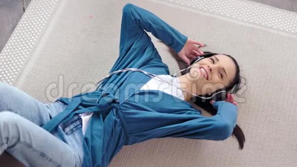 俯视图美丽的微笑女孩听音乐手拿耳机躺在地上视频的预览图