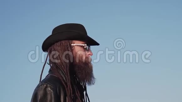 一个穿着黑色斗篷戴着帽子戴着黑色眼镜的人在桥上留着胡子和可怕的东西在阳光下眺望远方视频的预览图