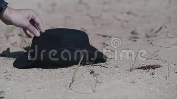 穿着雨衣戴着可怕帽子的酷家伙把帽子放在沙漠里开始用刀子在地上画东西视频的预览图