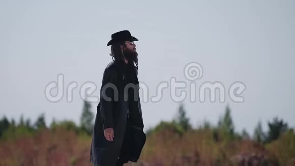 长焦镜头跟随着一个穿着黑色雨衣和帽子的人穿过沙漠视频的预览图
