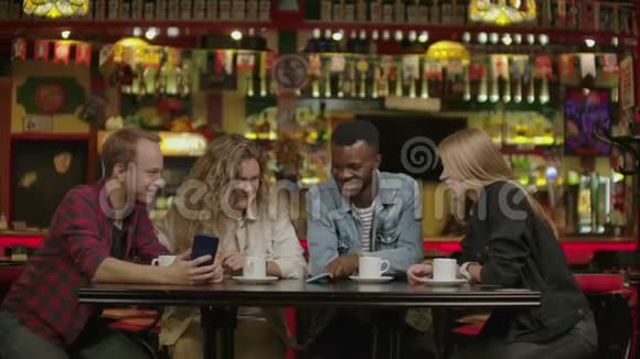 漂亮的西班牙裔男人在她的智能手机上向她的朋友展示有趣的东西而他们在酒吧玩得很开心他们视频的预览图