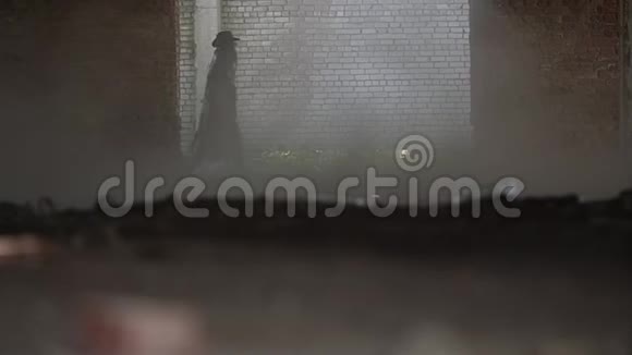 一个穿着黑色斗篷的男人的神秘身影正在镜头方向的一个尘土飞扬的房间上视频的预览图